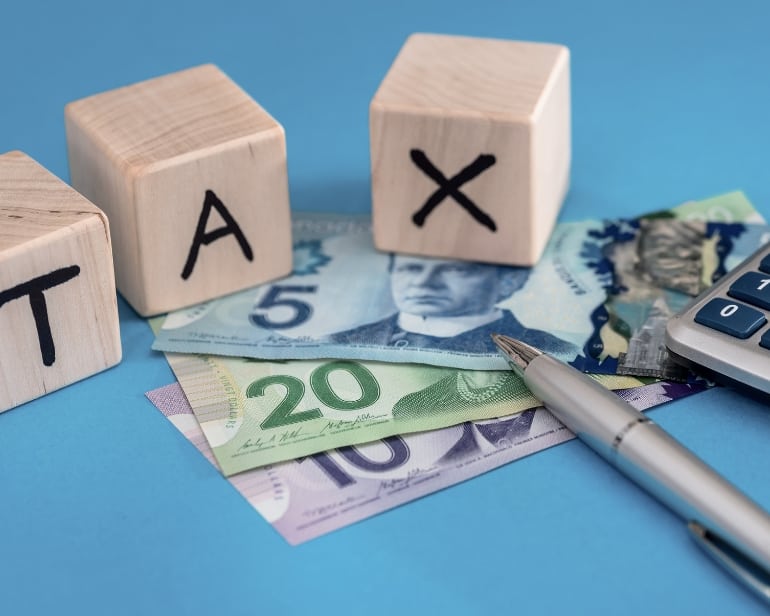 Wooden blocks spelling tax on top of Canadian Currency including $5, $10, & $20.