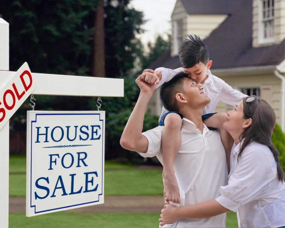 Happy family in front of house next to sold for sale sign.