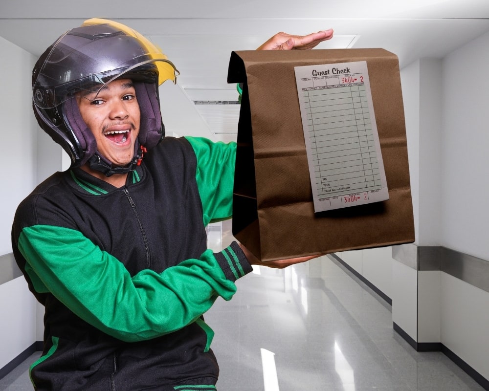 Happy Uber Eats driver wearing helmet, holding bag of take out food.