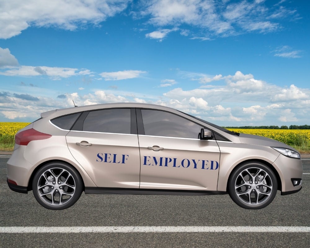 Vehicle on road with Self Employed on the side, with a sunny background.